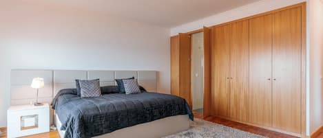 A bedroom with a bed, a nightstand, a lamp, a wardrobe, and a carpet.