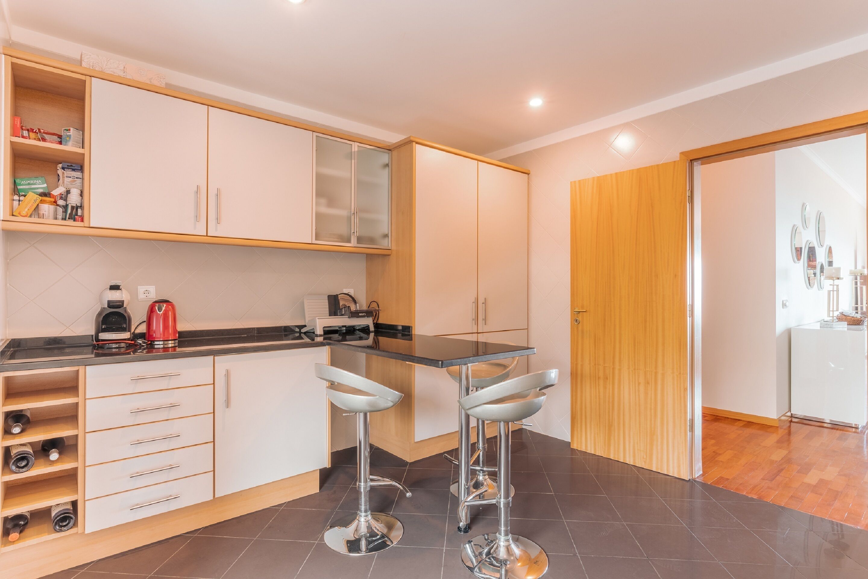 A modern kitchen with white cabinets, a black countertop, and two bar stools.