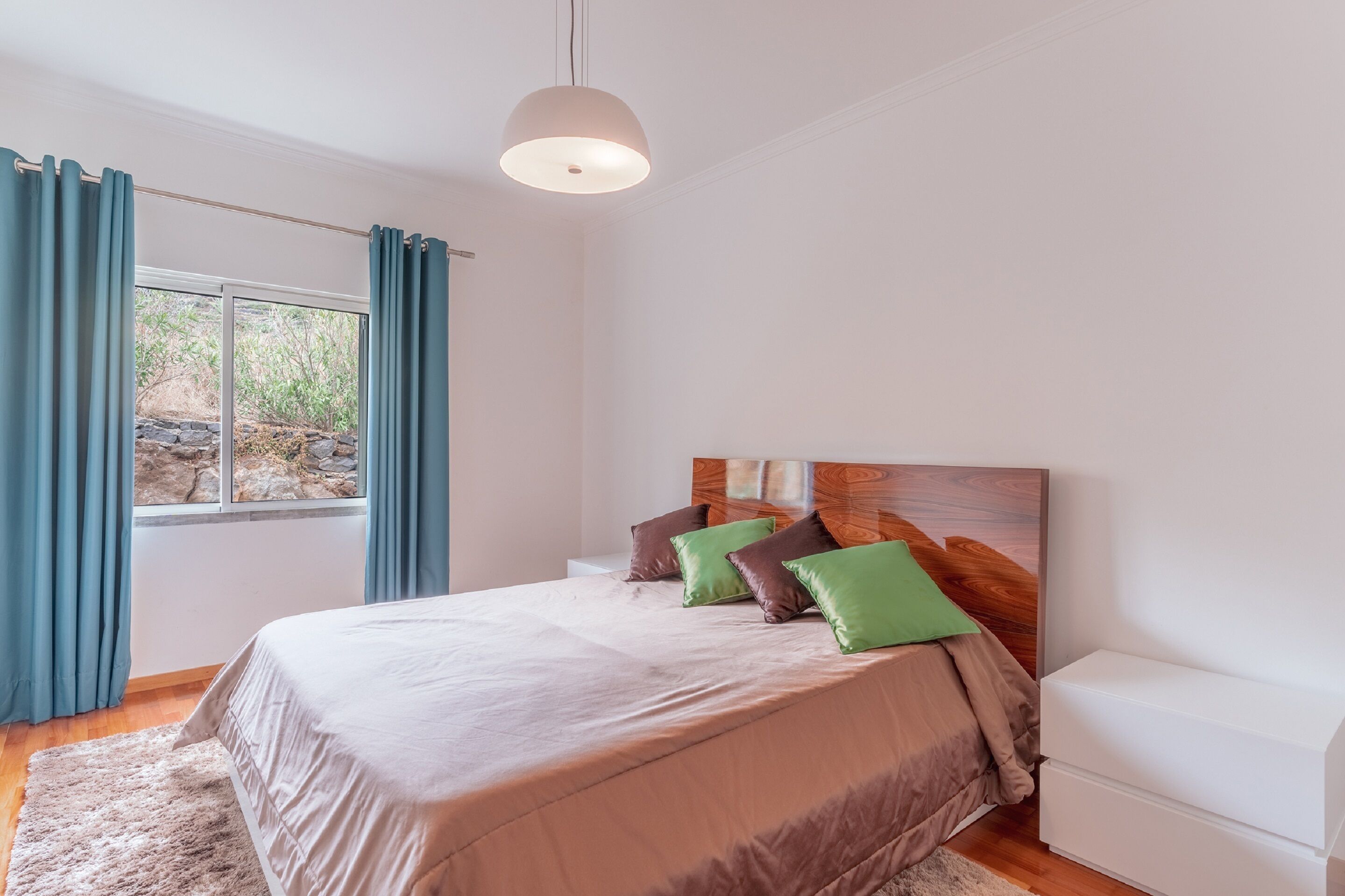 A bedroom with a bed, a nightstand, a window with curtains, and a pendant light.