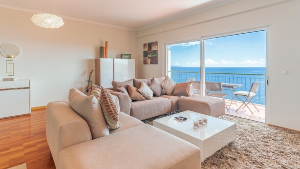 Ein modernes Wohnzimmer mit einer großen Couch, einem Couchtisch und Meerblick durch eine Schiebetür.