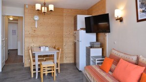 A compact living space with a dining area, kitchenette, and a sofa with orange cushions. - travelski home select - Résidence Licorne - 2 pièces 5 personnes (La Plagne)