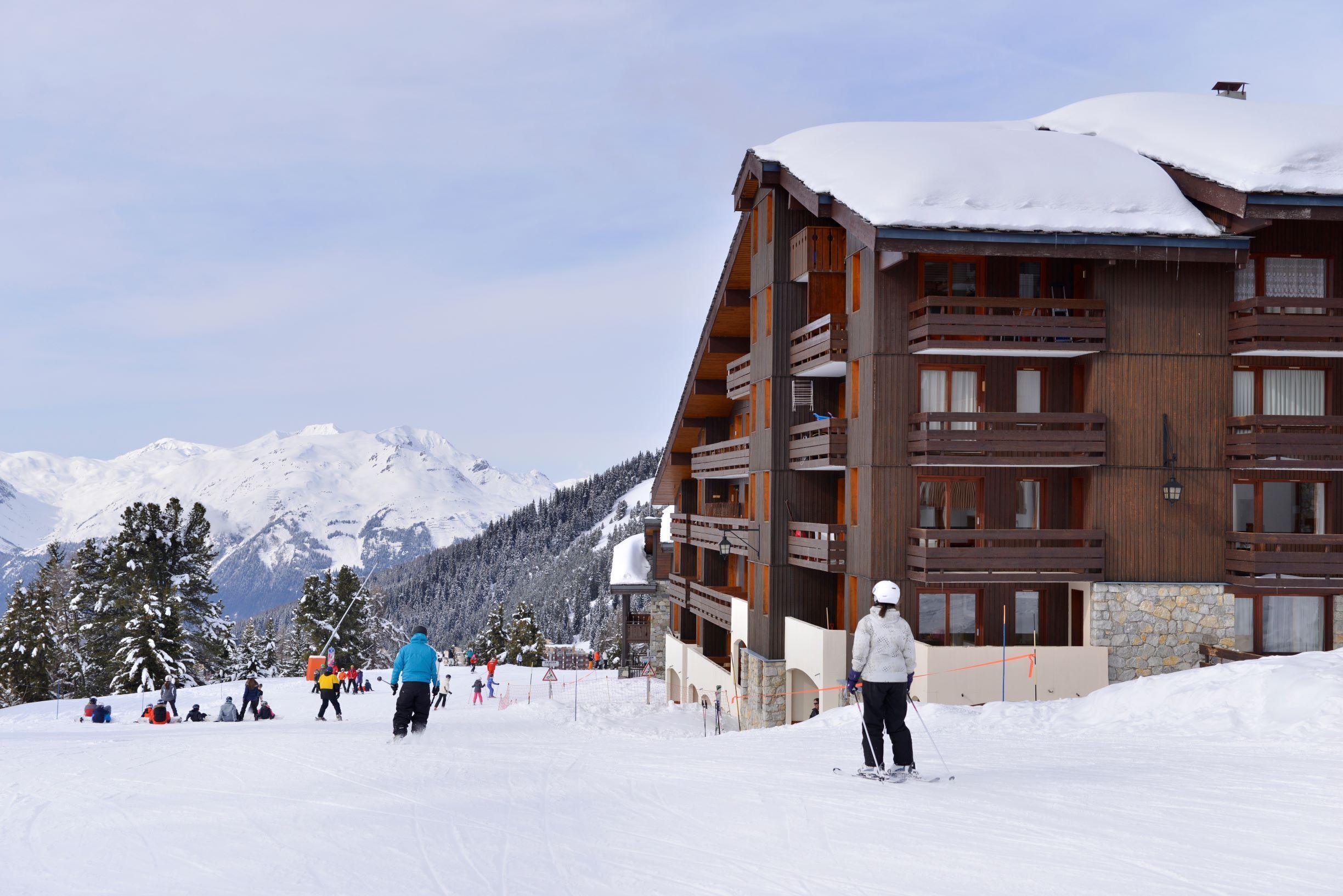 A multi-story wooden building with balconies, surrounded by snow-covered mountains.