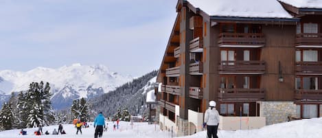 A multi-story wooden building with balconies, surrounded by snow-covered mountains.