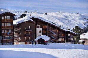 Een chalet bedekt met sneeuw, met meerdere balkons en een piste op de achtergrond.