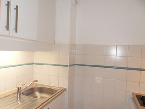 Cozinha com azulejos brancos, uma pia de aço inoxidável e armários de madeira.