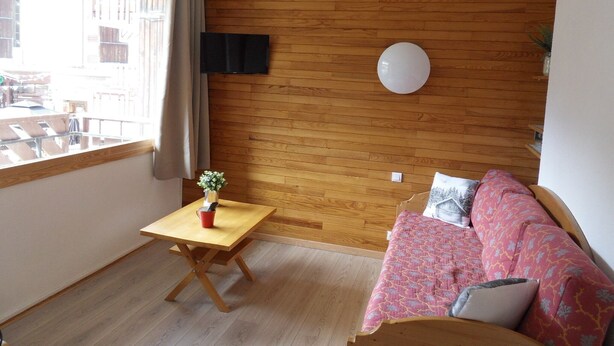 Une pièce aux murs lambrés, avec un plancher en bois, une petite table sur laquelle se trouve une tasse rouge, un canapé agrémenté de coussins à motifs et un luminaire rond.