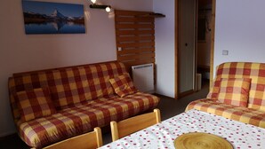 Una habitación acogedora con un sofá a cuadros, una mesa de comedor con mantel estampado de cerezas y un reloj colgado en la pared.