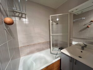 A modern bathroom with a bathtub, a glass shower enclosure, and a vanity with a mirror. - travelski home classic - Résidence Saint Jacques - 2 pièces 5 personnes (La Plagne)