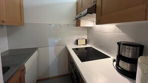 Una cocina compacta con armarios de madera, una placa de inducción negra, una cafetera y un tostador.