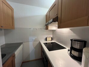 A compact kitchen with wooden cabinets, a black induction cooktop, a coffee maker, and a toaster. - travelski home classic - Résidence Saint Jacques - 2 pièces 5 personnes (La Plagne)