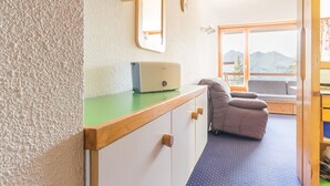 Een kamer met een houten bureau, een laptop, een comfortabele fauteuil en uitzicht op bergen door grote ramen.