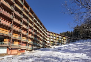 A multi-story hotel with balconies, set against a snowy landscape with trees and a clear sky.