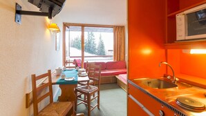 A compact kitchen with a sink, stove, and dining area with chairs and a table. - travelski home classic - Résidence Grand Arbois - Studio 4 personnes n°621 (Les Arcs)