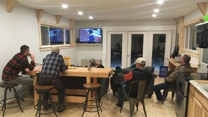 A group of people seated around a wooden table in a room with two televisions mounted on the wall. - Mountain View Motel & Campground (Stratton)