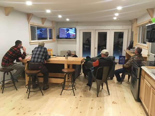 A group of people seated around a wooden table in a room with two televisions mounted on the wall. - Mountain View Motel & Campground (Stratton)