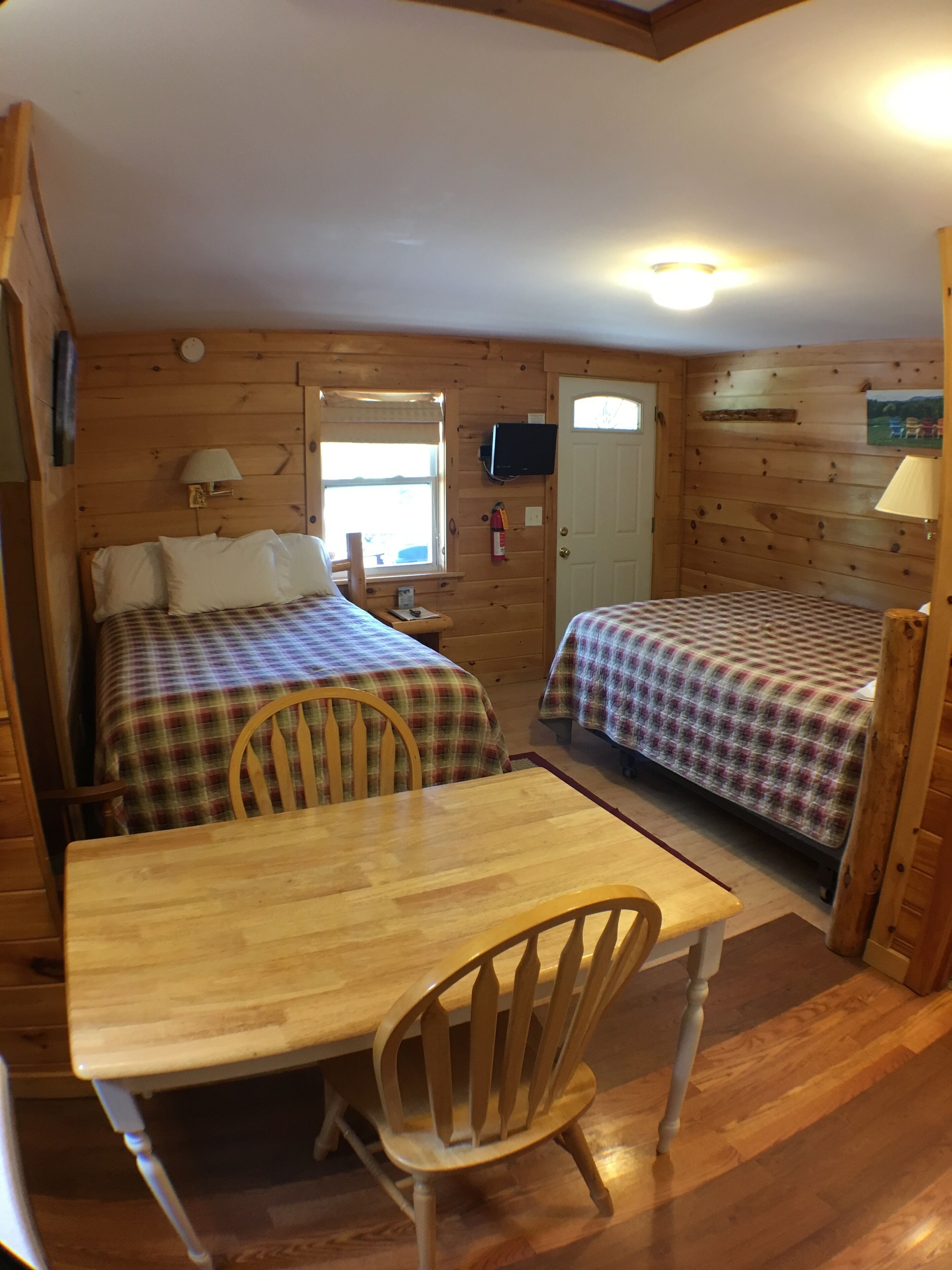 A cabin-style room with two beds, a wooden table, and a chair.