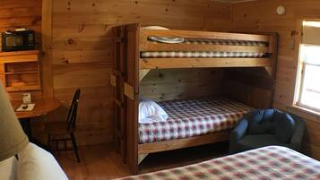 A bunk bed with a checkered bedspread, a desk with a chair, a microwave, and a window with natural light.