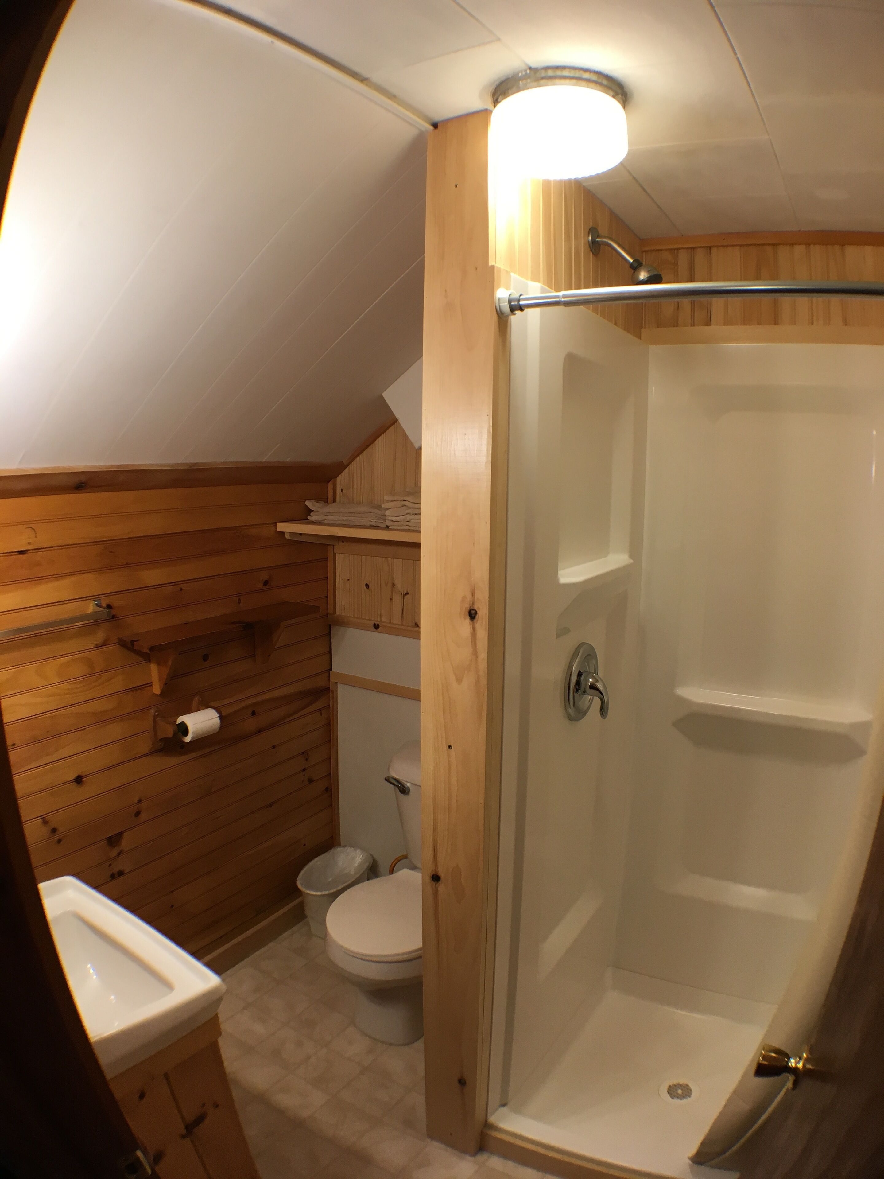 Un baño pequeño de madera con un inodoro, ducha y lavamanos.