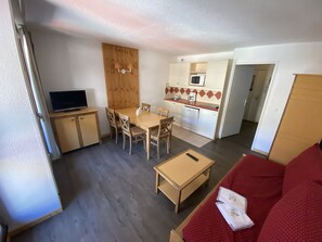 Ein kompakter Wohnraum mit Essbereich, Küchenzeile und einem roten Sofa.