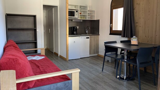 Un espacio habitable compacto con kitchenette, comedor y un sofá rojo.