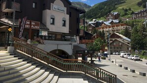 Un edificio con la señalización 'La Muzelle' y una escalera que sube a un nivel superior, rodeado de otros edificios y un paisaje montañoso.