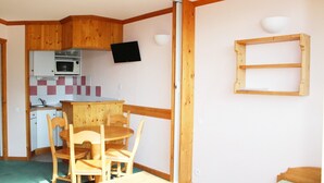 Una cocina compacta con microondas, una mesa de comedor de madera con sillas y un televisor montado en la pared.