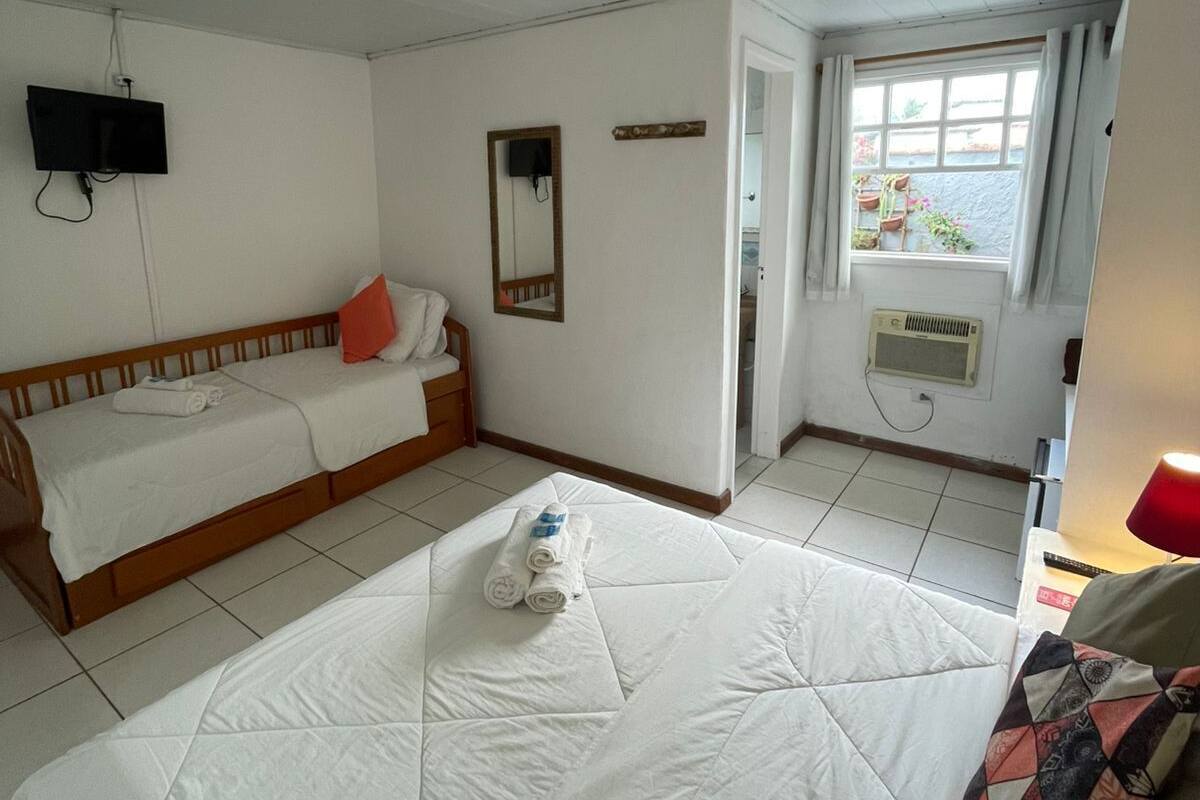 A room with a large bed, a smaller sofa, a TV mounted on the wall, and a window with curtains.