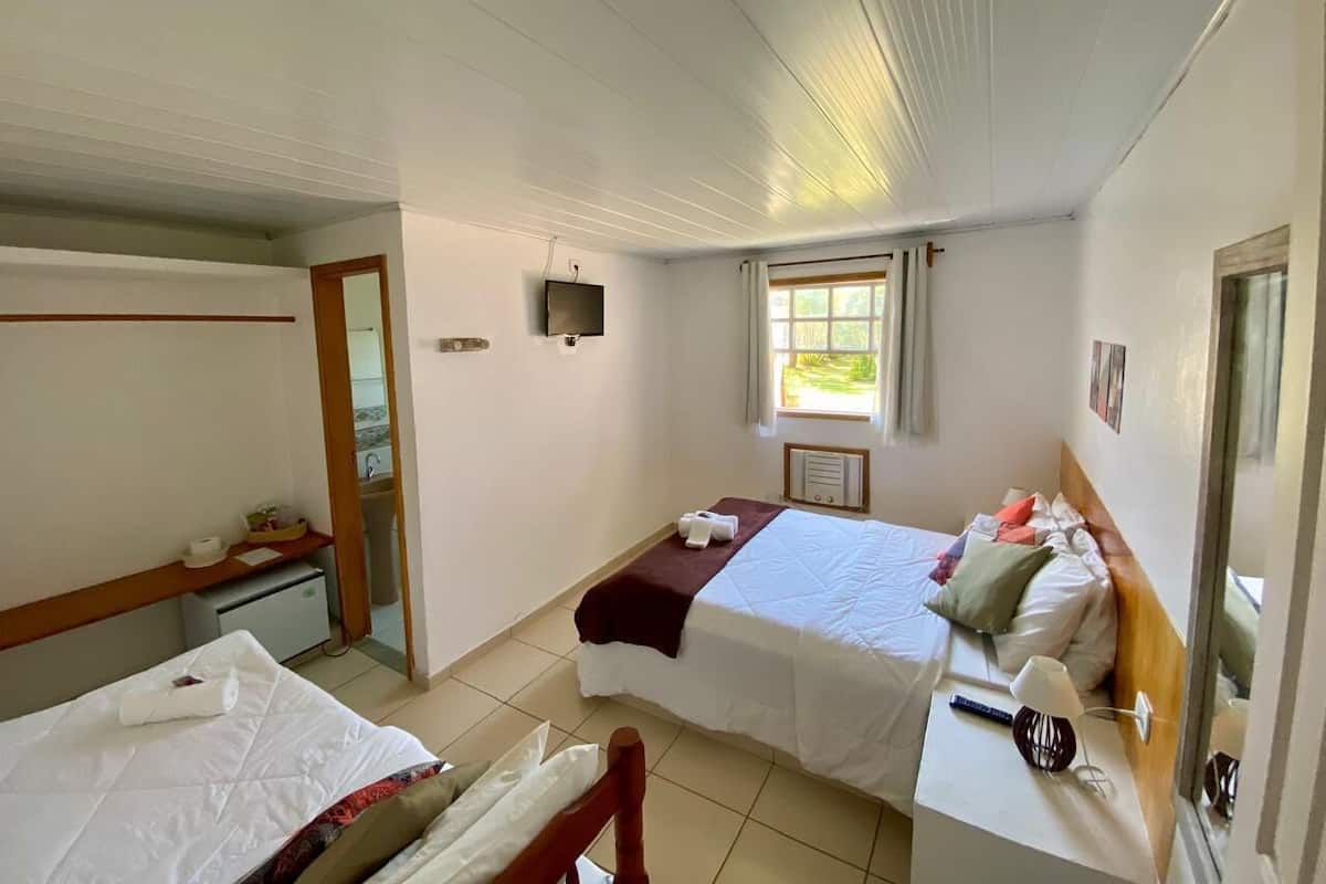 A hotel room with two beds, a desk, a mirror, a window, and a door.