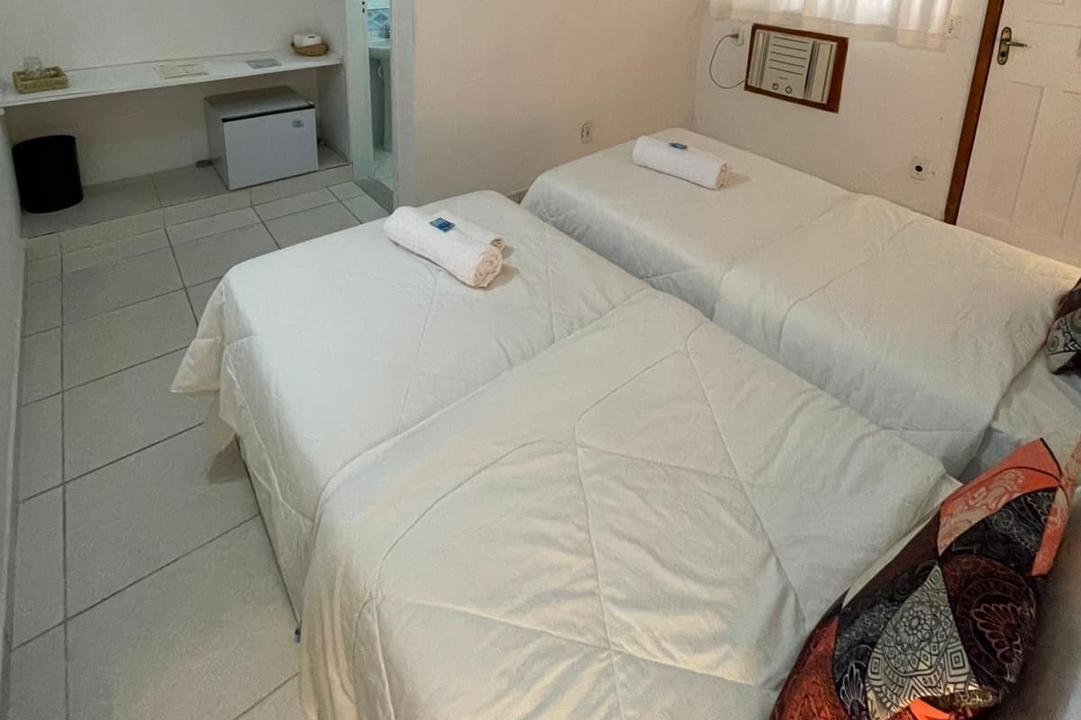 A hotel room with two beds, a desk, a small cabinet, a TV, and a window with curtains.