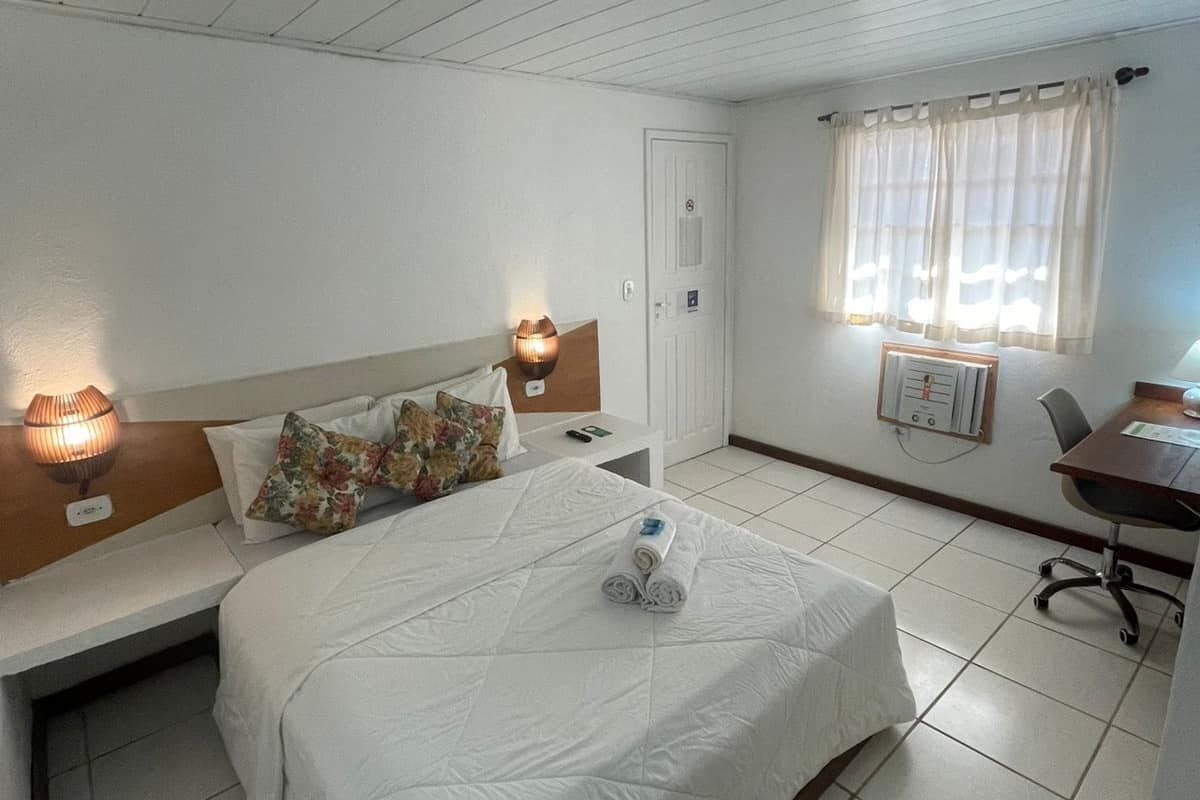 A hotel room with a bed, bedside tables, a desk, and a window with curtains.