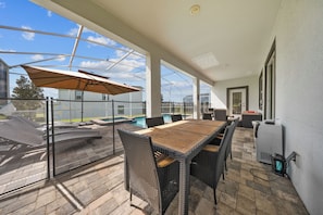 An outdoor patio with a pool, wicker furniture, and a glass enclosure.