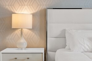 Une table de chevet blanche avec une lampe et un lit doté d’une tête de lit.