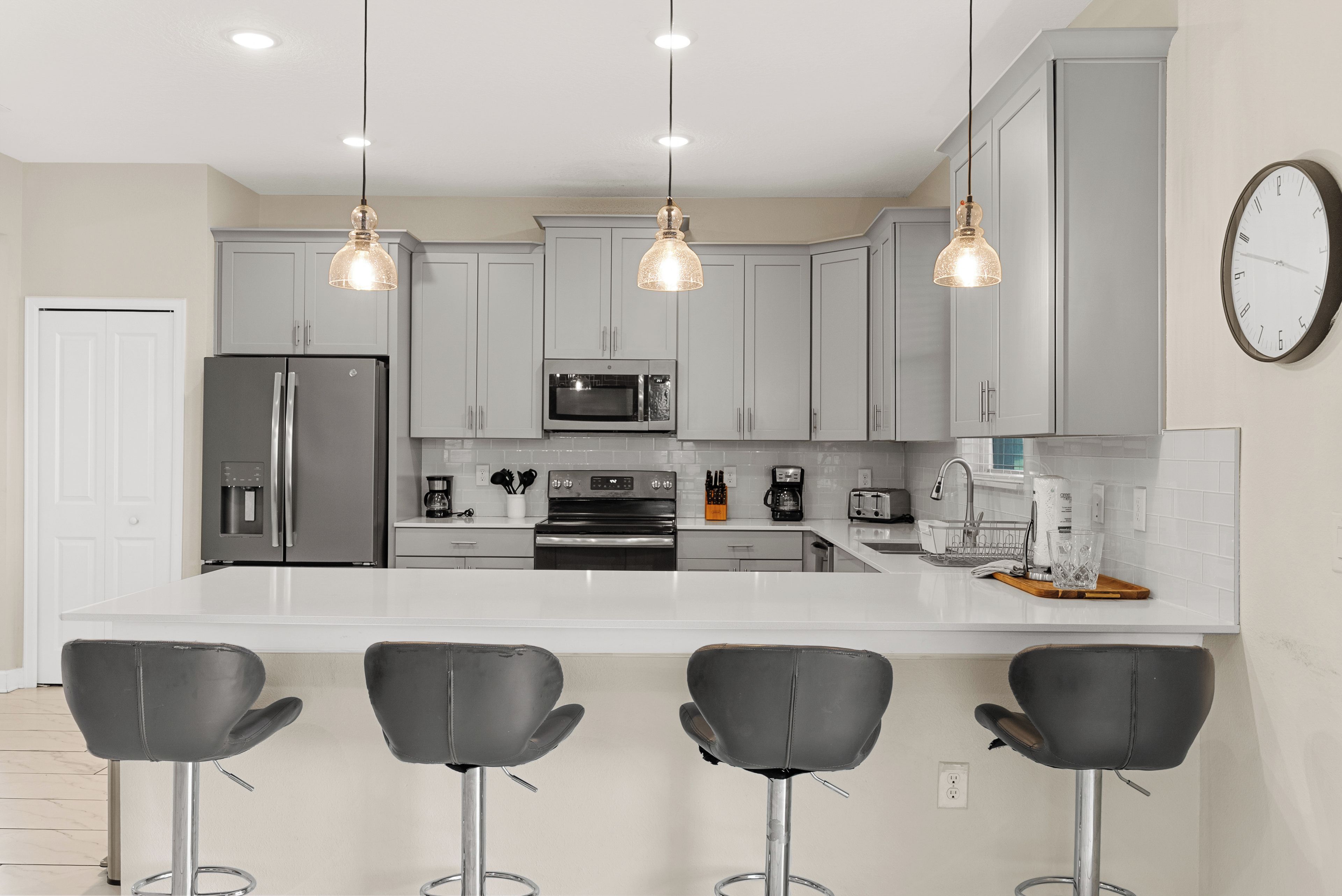 A modern kitchen with grey cabinets, stainless steel appliances, and pendant lighting.