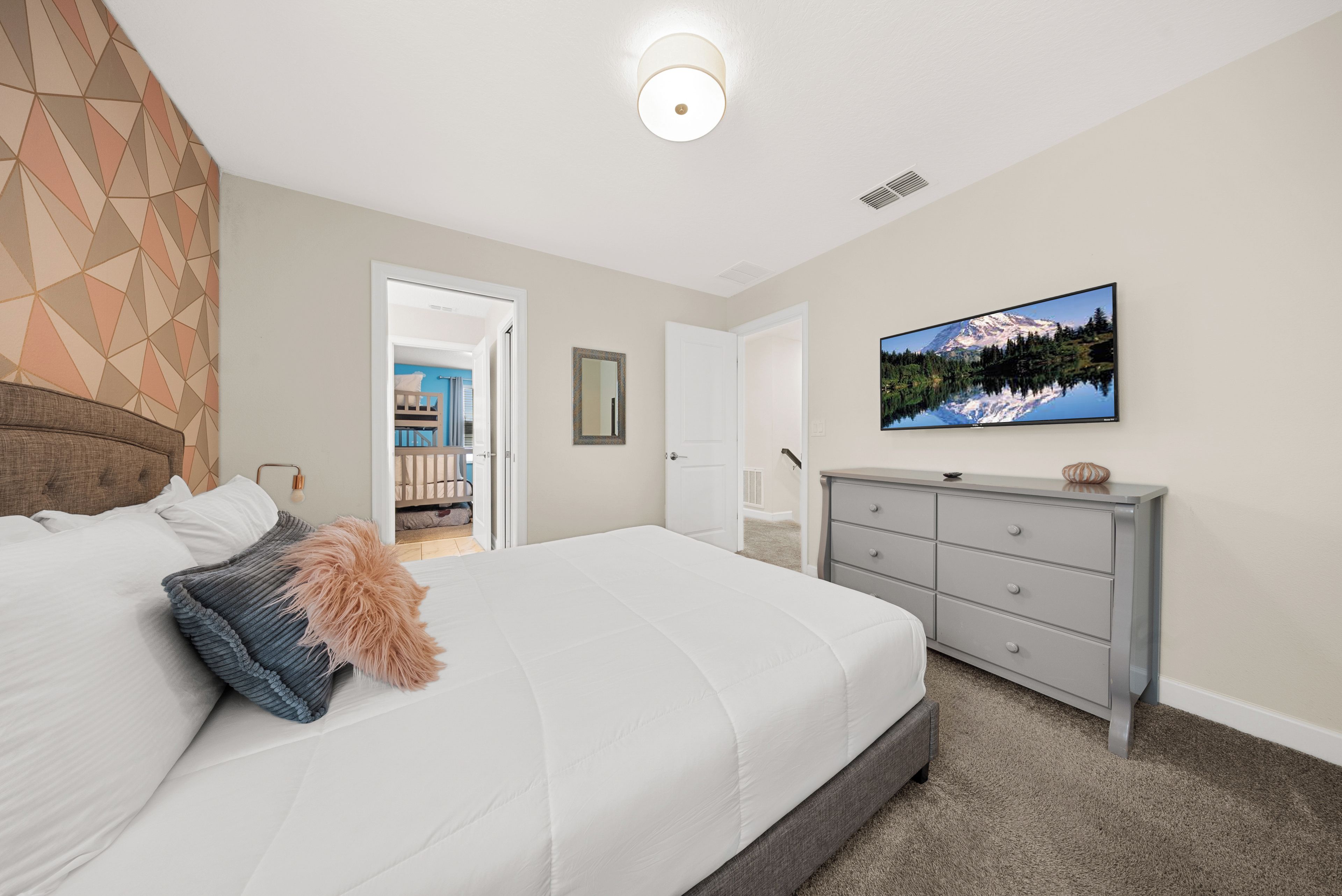 A bedroom with a bed, dresser, and a television on the wall.
