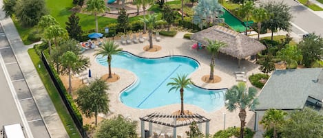 A swimming pool with a thatched-roof pavilion, surrounded by palm trees and lounge chairs.