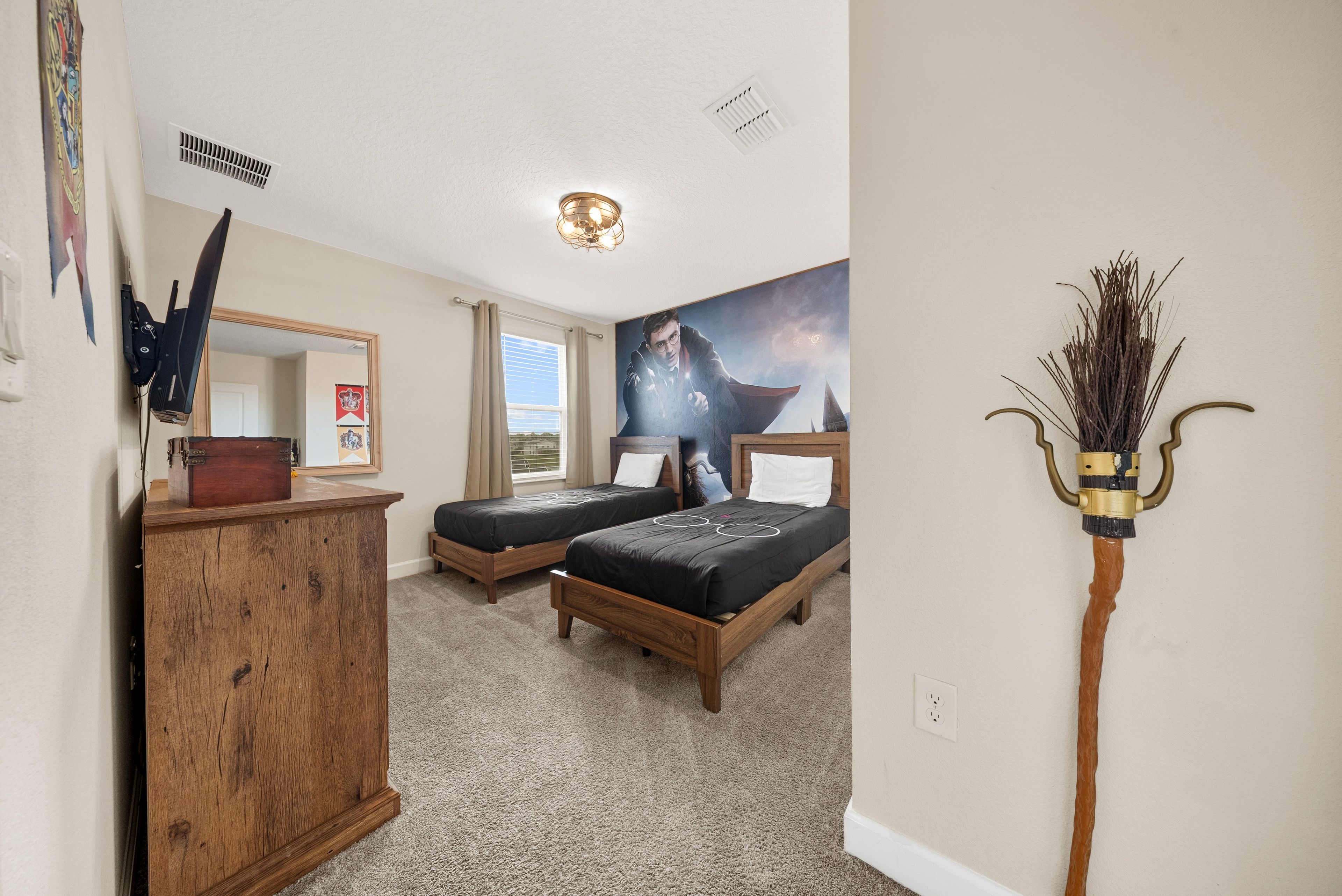 A bedroom with two wooden beds, a wooden dresser, a mirror, a ceiling light, and a wall-mounted decorative item.