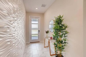 A hallway with a textured wall, a glass door, a mirror, a potted plant, and a small table with a vase.