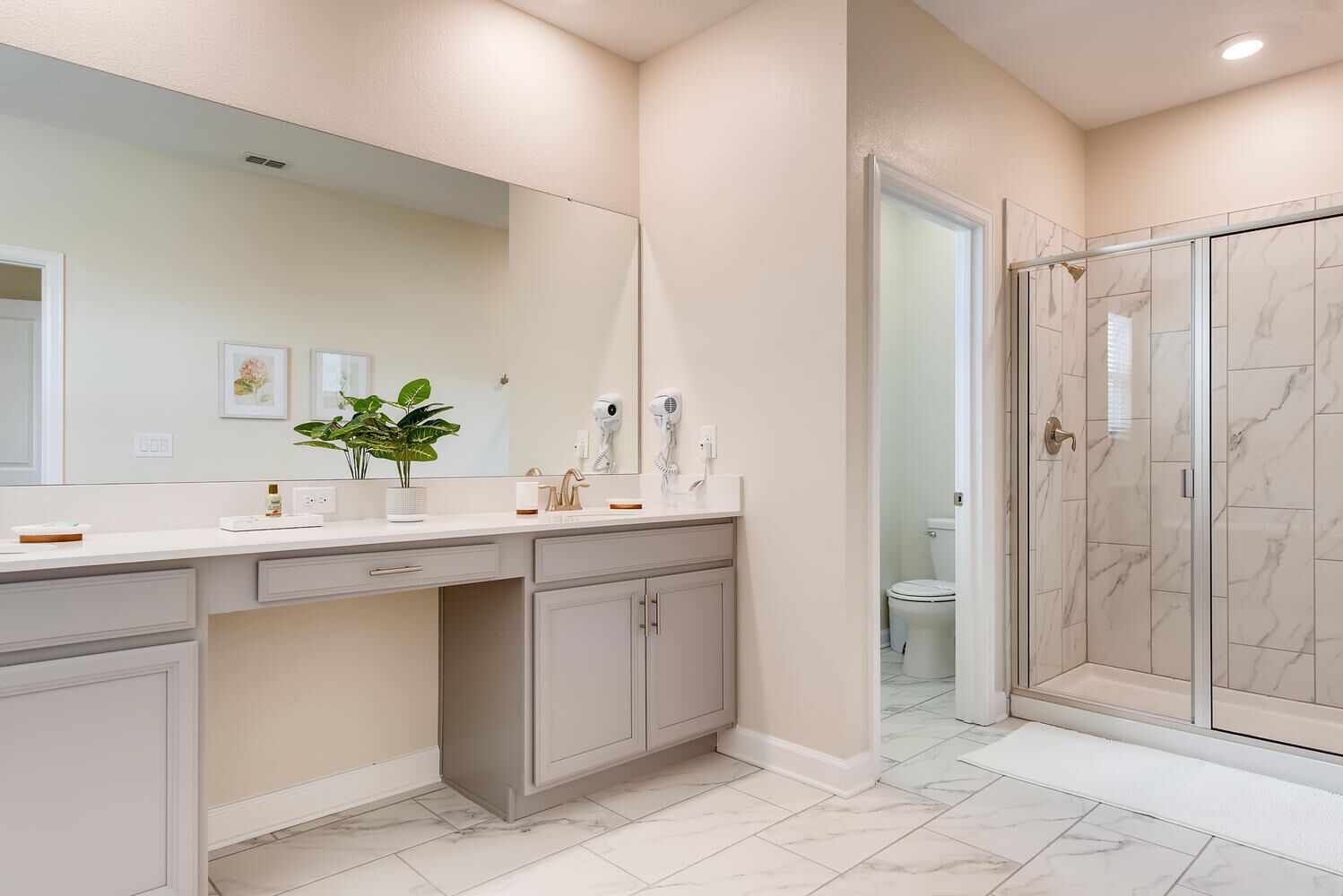 Une salle de bain avec un double vasque, un miroir, une plante et un espace douche.