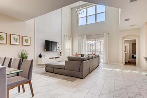 A spacious living room with a large sectional sofa, a flat-screen TV, and a dining area with chairs and a glass table.
