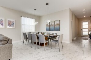 A modern dining area with a marble floor, a glass-top table, and grey upholstered chairs.