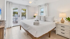 A spacious bedroom with a large bed, a ceiling fan, a nightstand with a lamp, and a view of the outdoors through a sliding glass door. - Magnolia walk to beach/shops, Ami perfect Location (Anna Maria)
