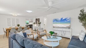 A modern living room with a large gray sofa, a dining area with a wooden table, and a kitchen in the background. - Magnolia walk to beach/shops, Ami perfect Location (Anna Maria)