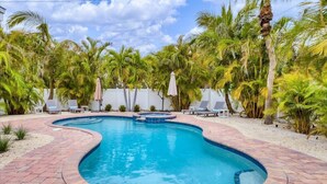 A swimming pool with a curved design, surrounded by palm trees and lounge chairs. - Magnolia walk to beach/shops, Ami perfect Location (Anna Maria)