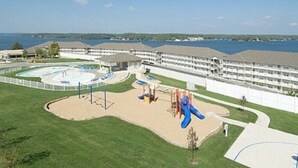 Un parque infantil con toboganes y estructuras para escalar, rodeado por una piscina y un edificio con varios balcones.