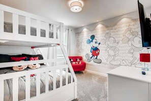 A child's room with bunk beds, a red chair, and a wall mural of Mickey Mouse.