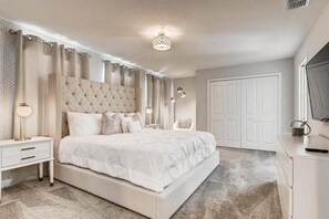 A bedroom with a large bed, a bedside table, a lamp, a wardrobe, and a television. - 2859 BD – Stunning Lakefront Pool Retreat at Storey Lake (Kissimmee)