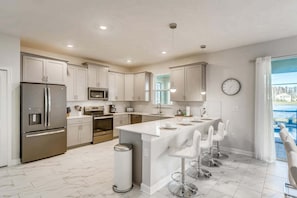 A modern kitchen with stainless steel appliances, a central island with bar stools, and a view of a swimming pool. - 2859 BD – Stunning Lakefront Pool Retreat at Storey Lake (Kissimmee)