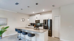 A modern kitchen with a central island, bar stools, stainless steel appliances, and pendant lighting. - 4321 QS - Magical Haven Townhome w/ Pool (Kissimmee)