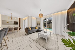 A modern living room with a grey sofa, a coffee table, and a dining area with chairs and a table. - 2929 SS - Disney Delight: 4BR, Pool, Near Parks (Kissimmee)