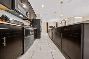 A modern kitchen with dark cabinetry, stainless steel appliances, and a tiled floor.